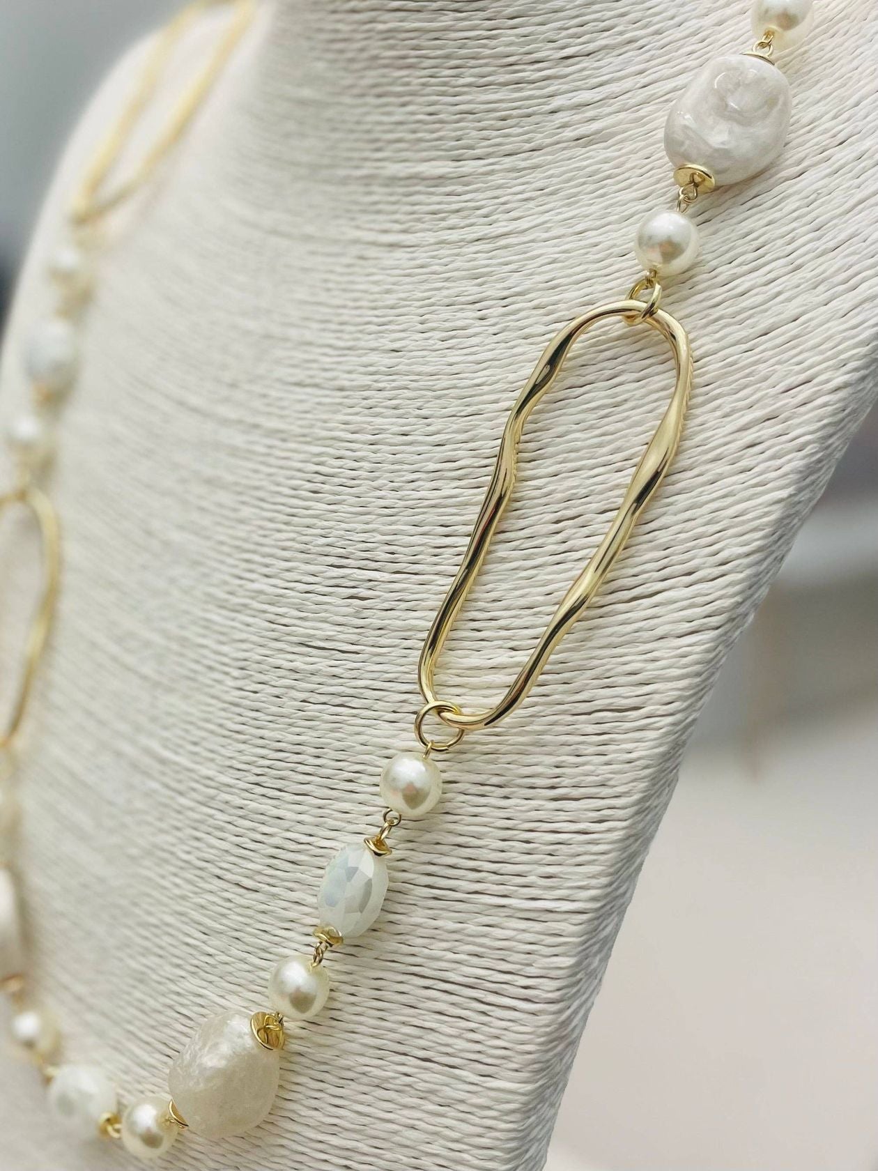 Long necklace with faux pearls and faceted stones draped on a display bust, showcasing layered textures
