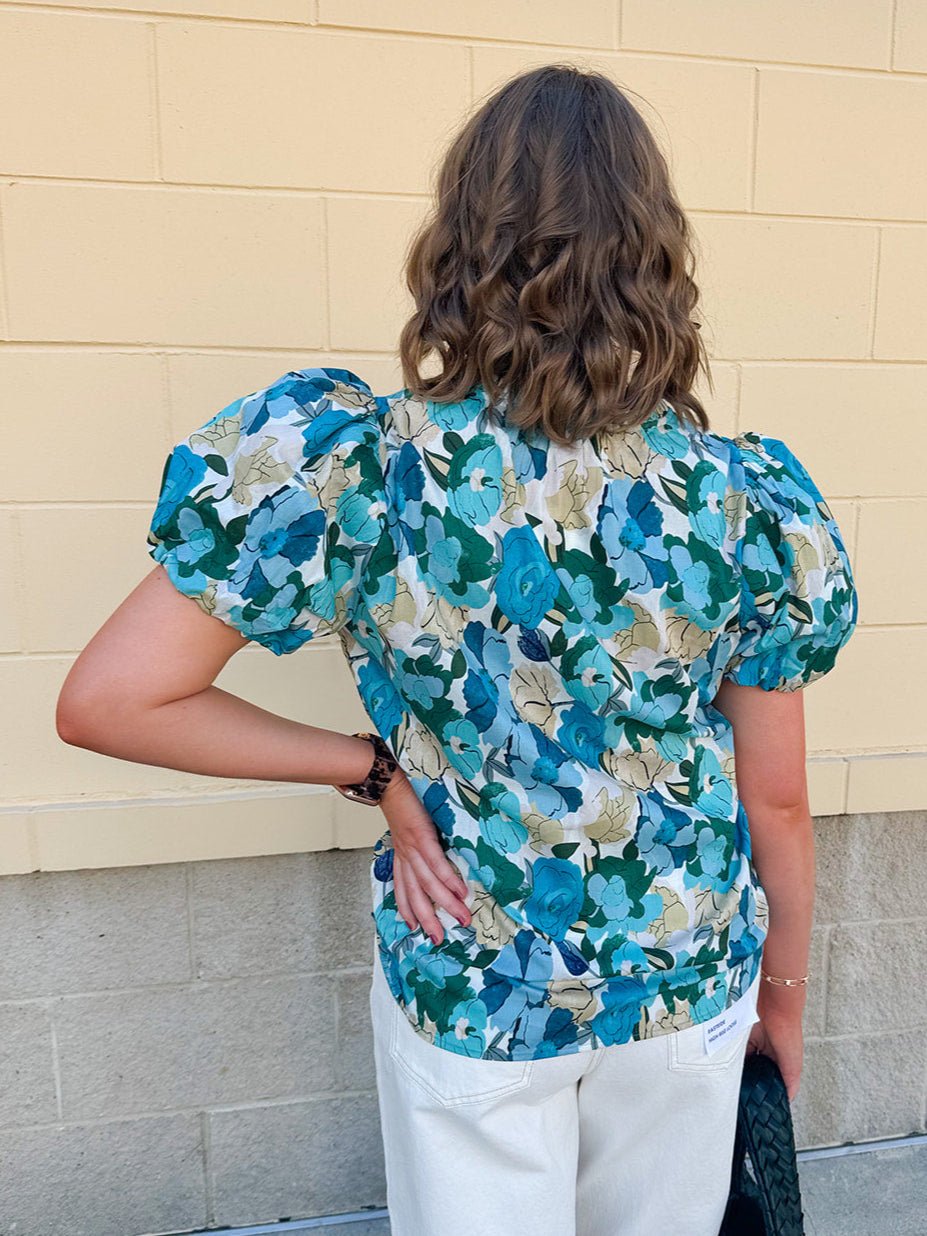 Blue floral blouse with pink accents, featuring a ruffle-trimmed split neckline and short puff sleeves