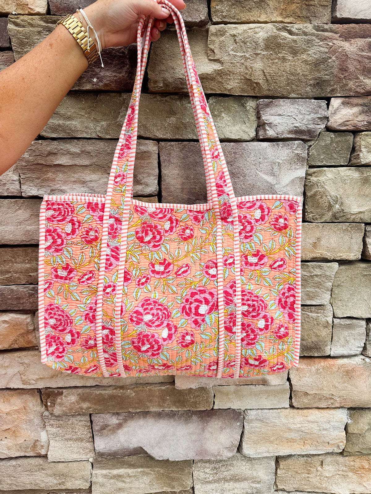 Quilted cotton tote bag in orange floral print with pink and green accents, reversible to an orange and pink mini floral pattern; features long shoulder straps and interior pocket.