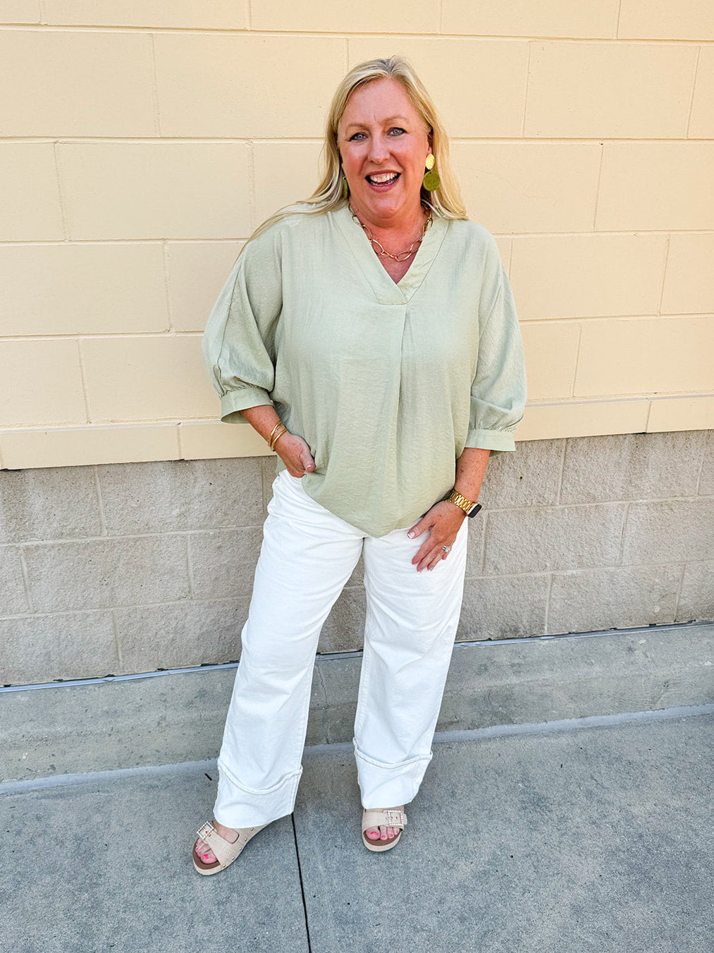 Sage green V-neck loose-fit blouse with pleated cuffed sleeves, styled for a fresh and effortless look.