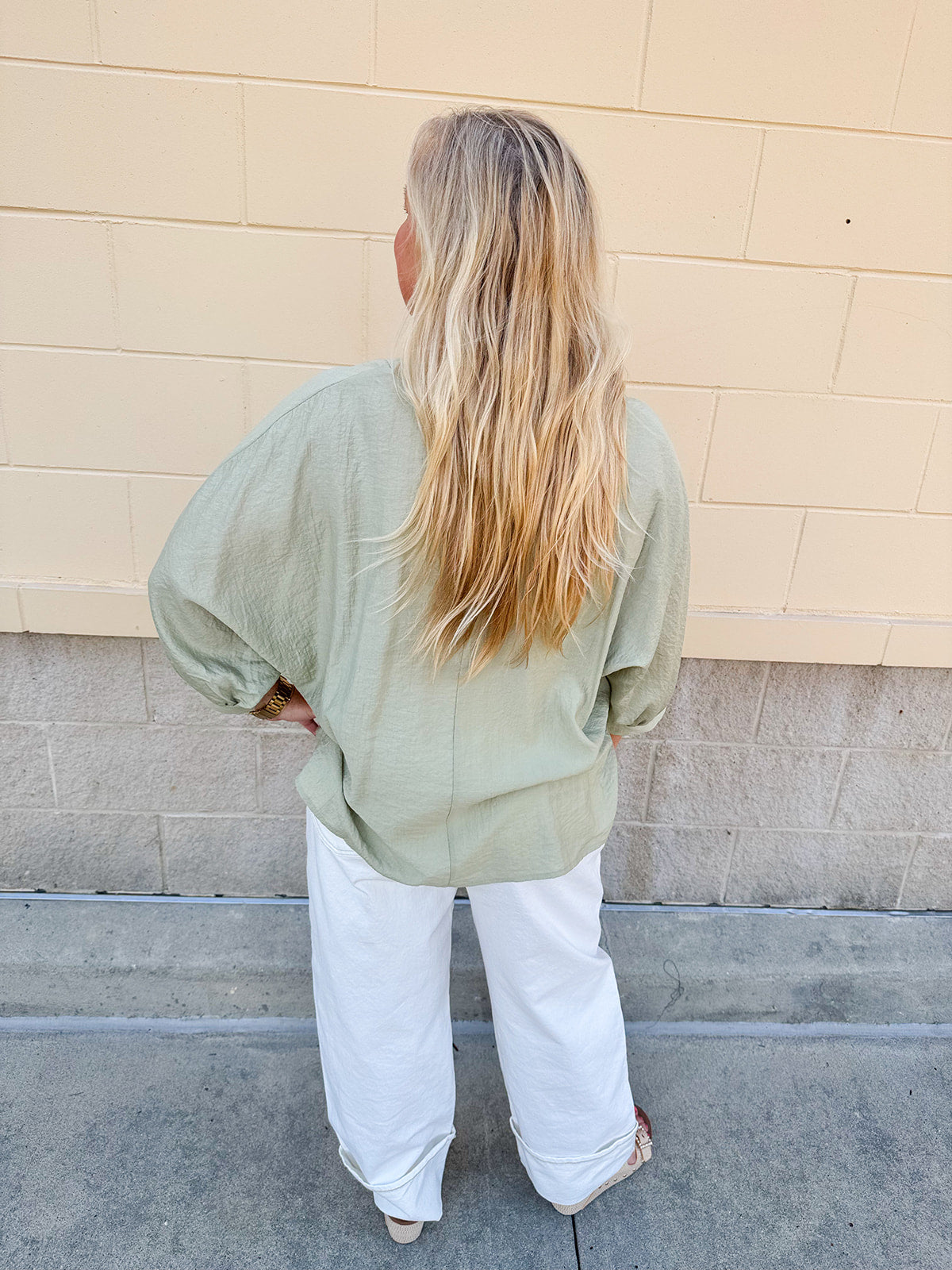 Sage green V-neck loose-fit blouse with pleated cuffed sleeves, styled for a fresh and effortless look.