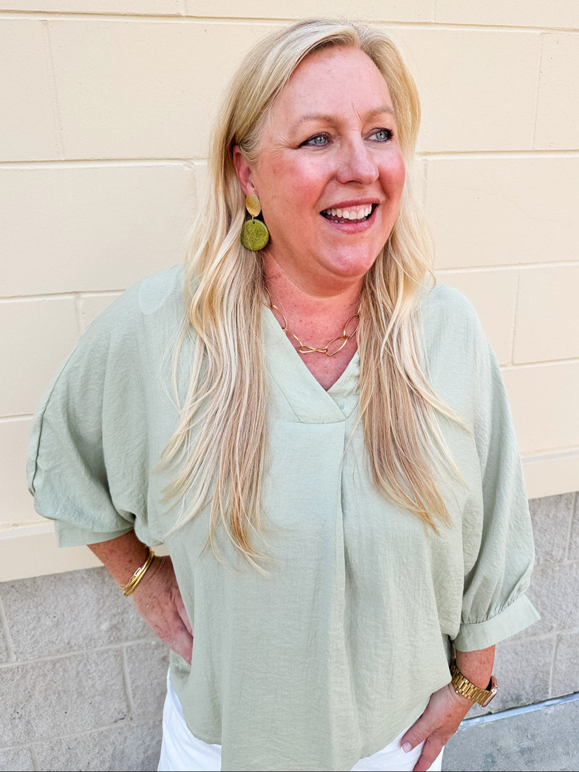Sage green V-neck loose-fit blouse with pleated cuffed sleeves, styled for a fresh and effortless look.