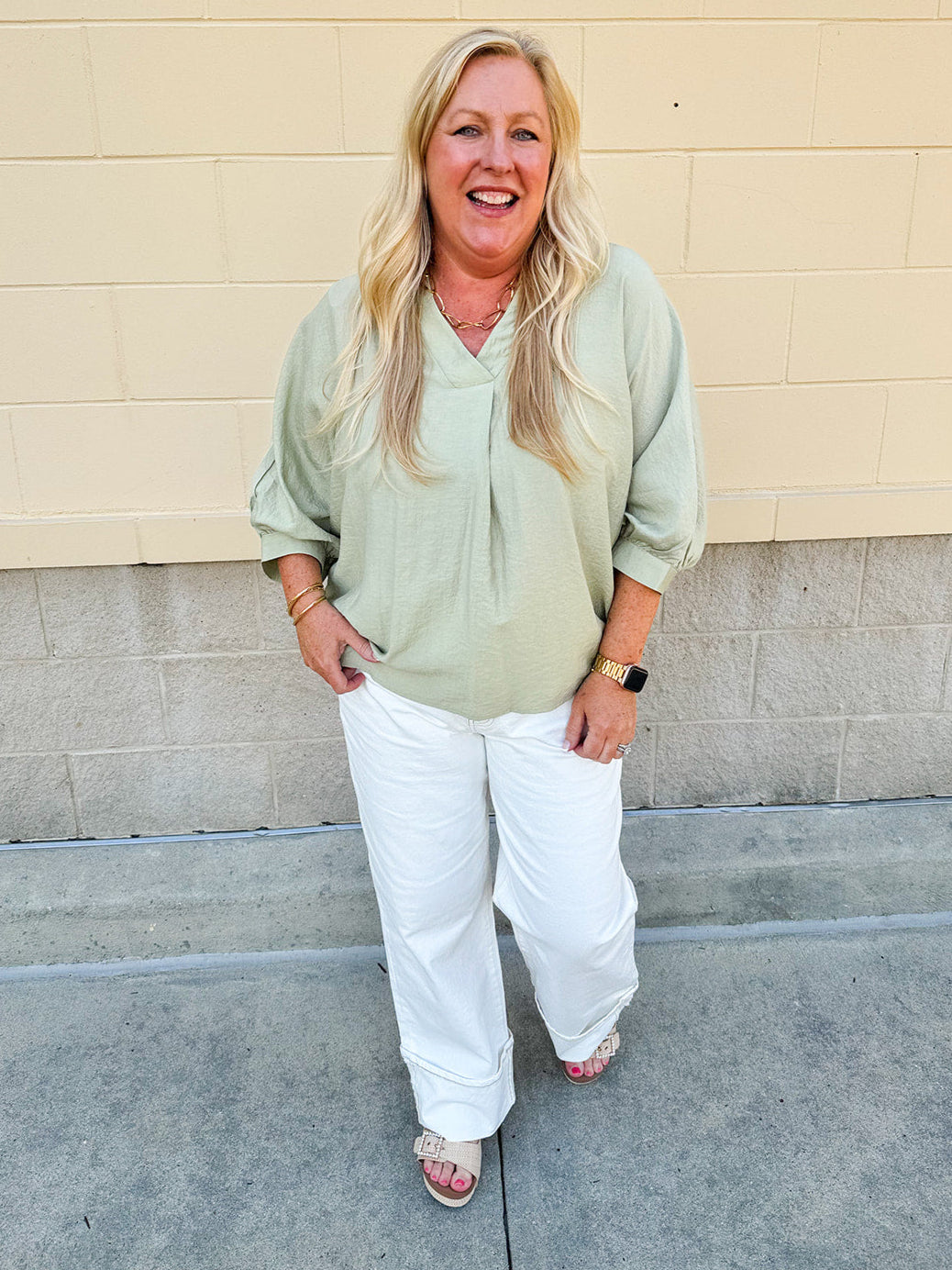 Sage green V-neck loose-fit blouse with pleated cuffed sleeves, styled for a fresh and effortless look.