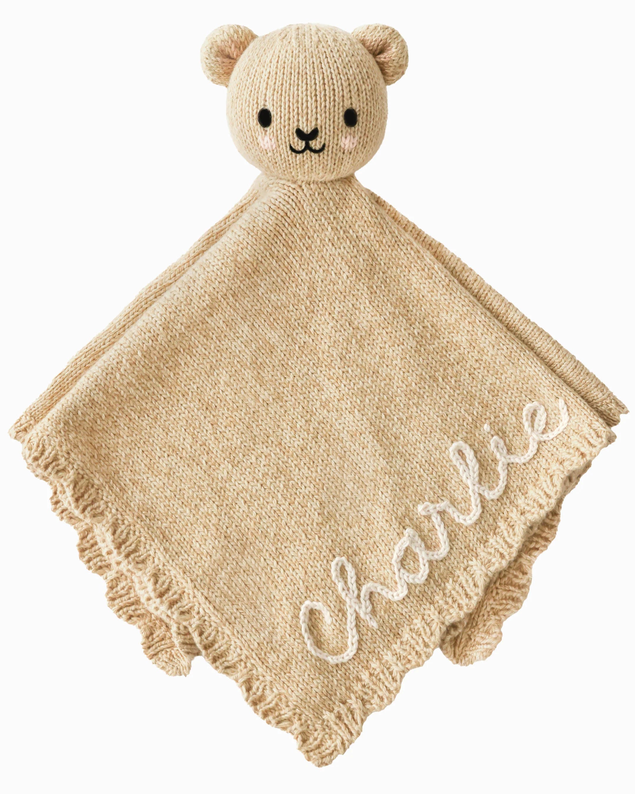 A honey-colored hand-knit baby lovey with scalloped trim and embroidered details.