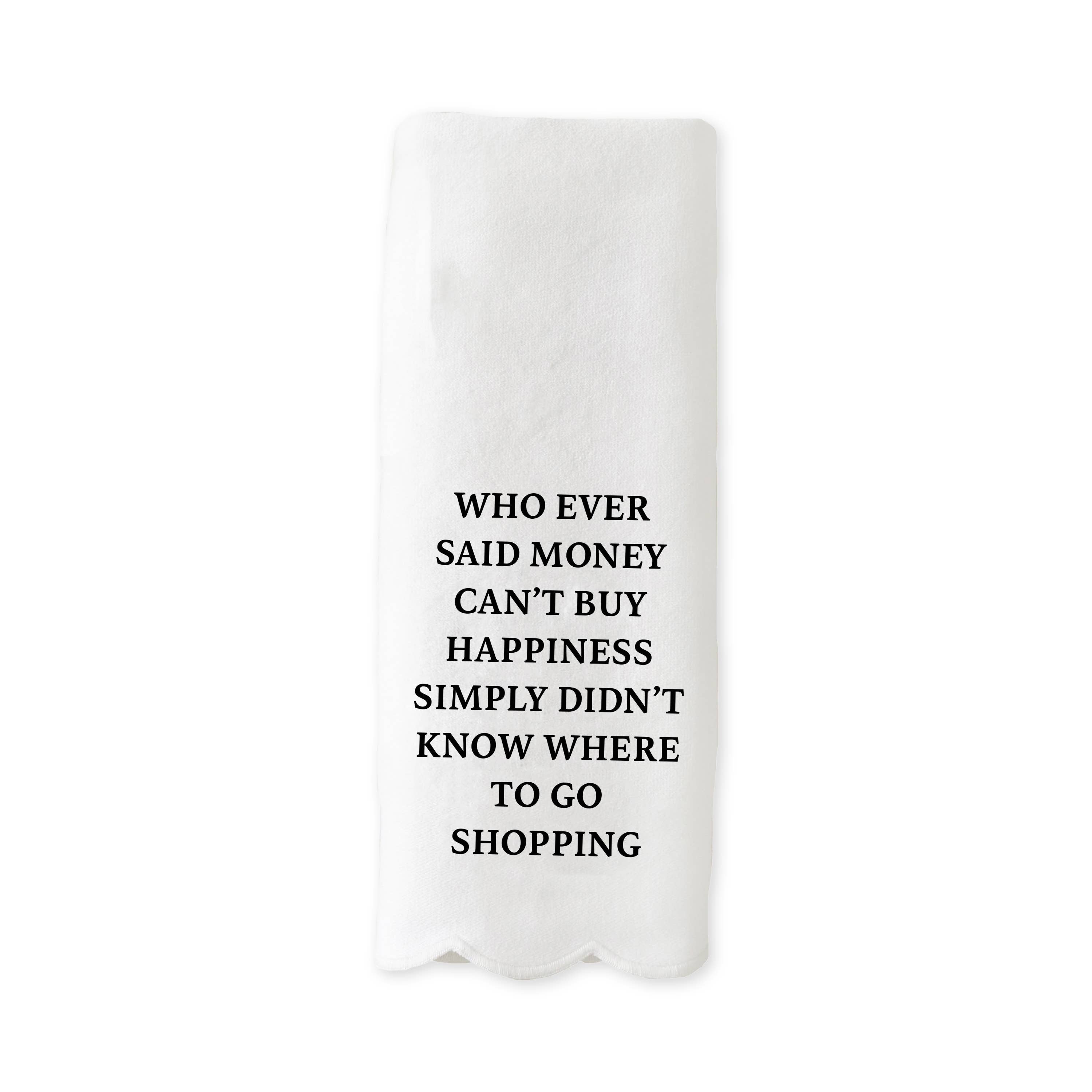 White scalloped-edge kitchen towel with black text reading “Whoever said money can’t buy happiness simply didn’t know where to go shopping.”