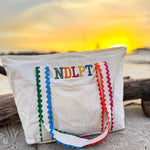 Lightweight canvas NDLPT project tote with embroidered design, colorful ric-rac shoulder straps, zip-top closure, and exterior pocket