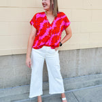 Banana and floral print top in orange and hot pink with V-neck and short dolman sleeves, displayed on hanger against neutral background