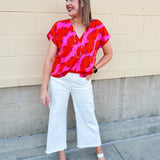 Banana and floral print top in orange and hot pink with V-neck and short dolman sleeves, displayed on hanger against neutral background