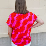 Banana and floral print top in orange and hot pink with V-neck and short dolman sleeves, displayed on hanger against neutral background