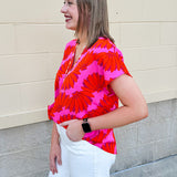 Banana and floral print top in orange and hot pink with V-neck and short dolman sleeves, displayed on hanger against neutral background