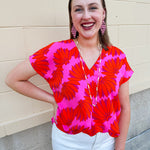Banana and floral print top in orange and hot pink with V-neck and short dolman sleeves, displayed on hanger against neutral background