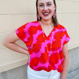 Banana and floral print top in orange and hot pink with V-neck and short dolman sleeves, displayed on hanger against neutral background