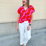 Banana and floral print top in orange and hot pink with V-neck and short dolman sleeves, displayed on hanger against neutral background