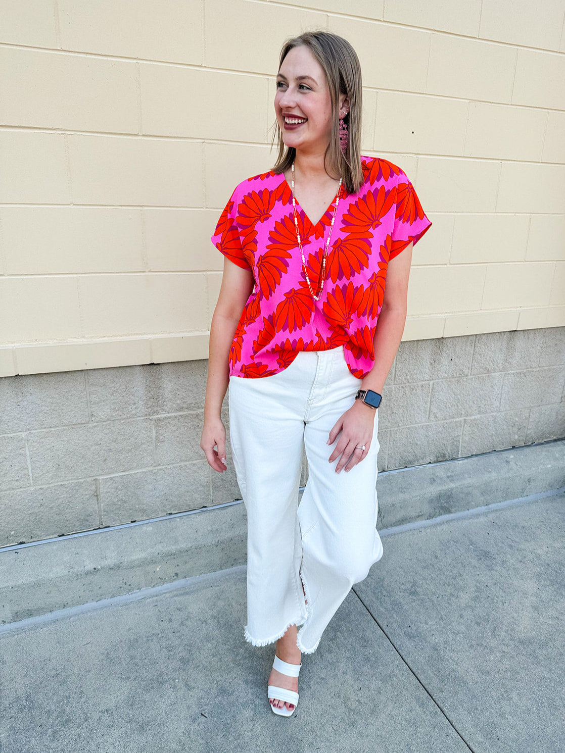 Banana and floral print top in orange and hot pink with V-neck and short dolman sleeves, displayed on hanger against neutral background