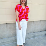 Banana and floral print top in orange and hot pink with V-neck and short dolman sleeves, displayed on hanger against neutral background
