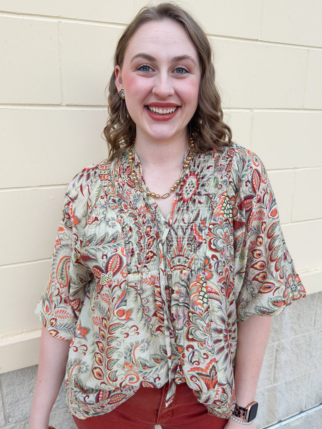 Brown, orange, and green printed smocked top with V-neck and tie neck