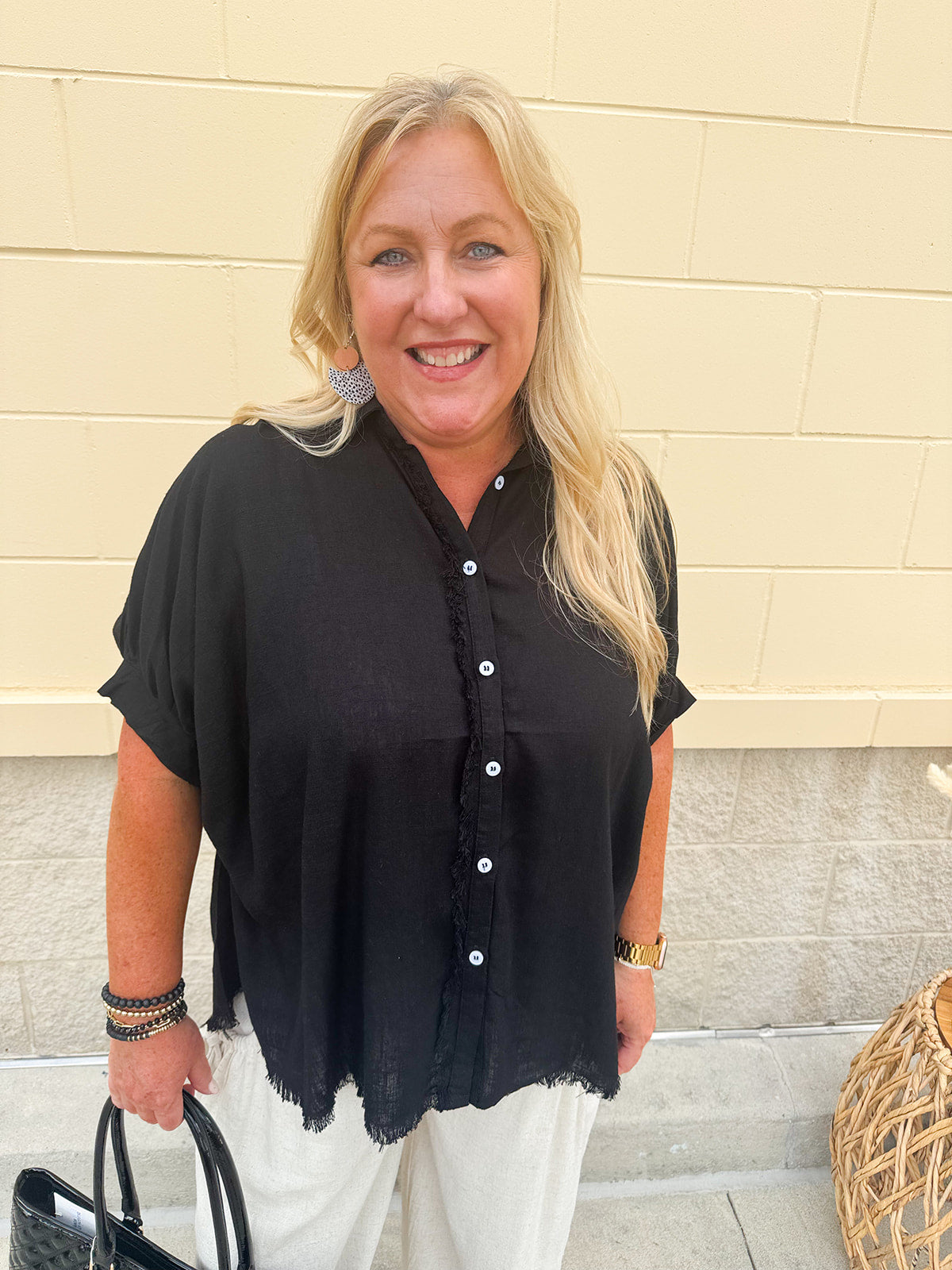 Solid black linen button-down shirt with rolled sleeves and frayed edge details, styled for easy summer layering.