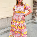 Blush pink and yellow floral print women’s midi dress with V-neckline, short puff sleeves, smocked elastic waist, and flowing skirt.