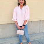Blush blouse with V-neckline, balloon sleeves, front pleat, and ruffle-trimmed cuffs