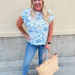 Blue paisley print cap sleeve blouse with round neckline and back button detail, styled for a soft and polished look.