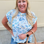 Blue paisley print cap sleeve blouse with round neckline and back button detail, styled for a soft and polished look.