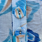 Blue paisley print cap sleeve blouse with round neckline and back button detail, styled for a soft and polished look.
