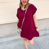 Garnet loose fit button-up dress with collared neckline, cuffed sleeves, front pockets, and relaxed silhouette.