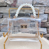 Clearly Handbags Audrey clear PVC crossbody bag with pearl wristlet handle, removable gold chain strap, and gold-plated hardware.