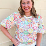 Women’s ivory printed top with colorful medallion pattern, short puff sleeves, ribbed crew neckline, ivory banded hem, and fringe trim.