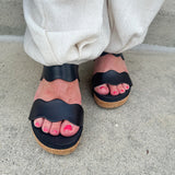 Black scalloped wedge sandals with cork sole, gold hardware accents, and dual straps—stylish and comfortable for everyday wear.