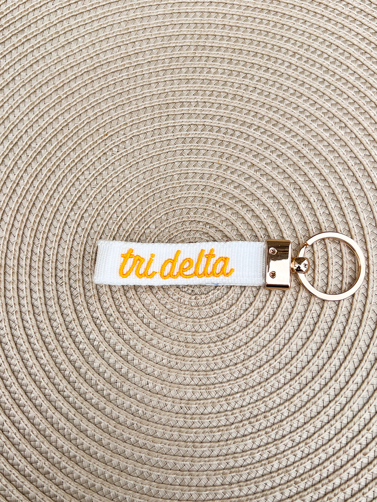 Double-sided embroidered Delta Delta Delta sorority keychain with white strap, signature color Greek letters, sorority name, and gold hardware.