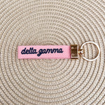 Double-sided embroidered Delta Gamma sorority keychain featuring Greek letters, script sorority name, and polished gold hardware.