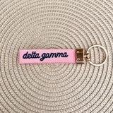 Double-sided embroidered Delta Gamma sorority keychain featuring Greek letters, script sorority name, and polished gold hardware.