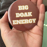 Round button in garnet with white and gold lettering that reads “Big Doak Energy.”