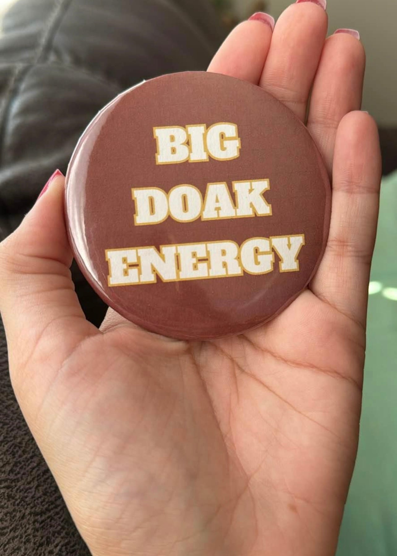 Round button in garnet with white and gold lettering that reads “Big Doak Energy.”