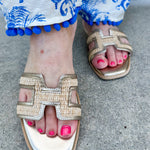 Ena Raffia H-Cutout Slides featuring a breathable raffia strap and modern H-cutout design, styled on a clean surface to showcase their chic, casual summer look and cushioned footbed