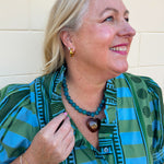 [Entro] Willow Embroidered Blouse featuring a green and light blue geometric pattern, V-neckline, puff sleeves, dark green trim, and embroidered details.