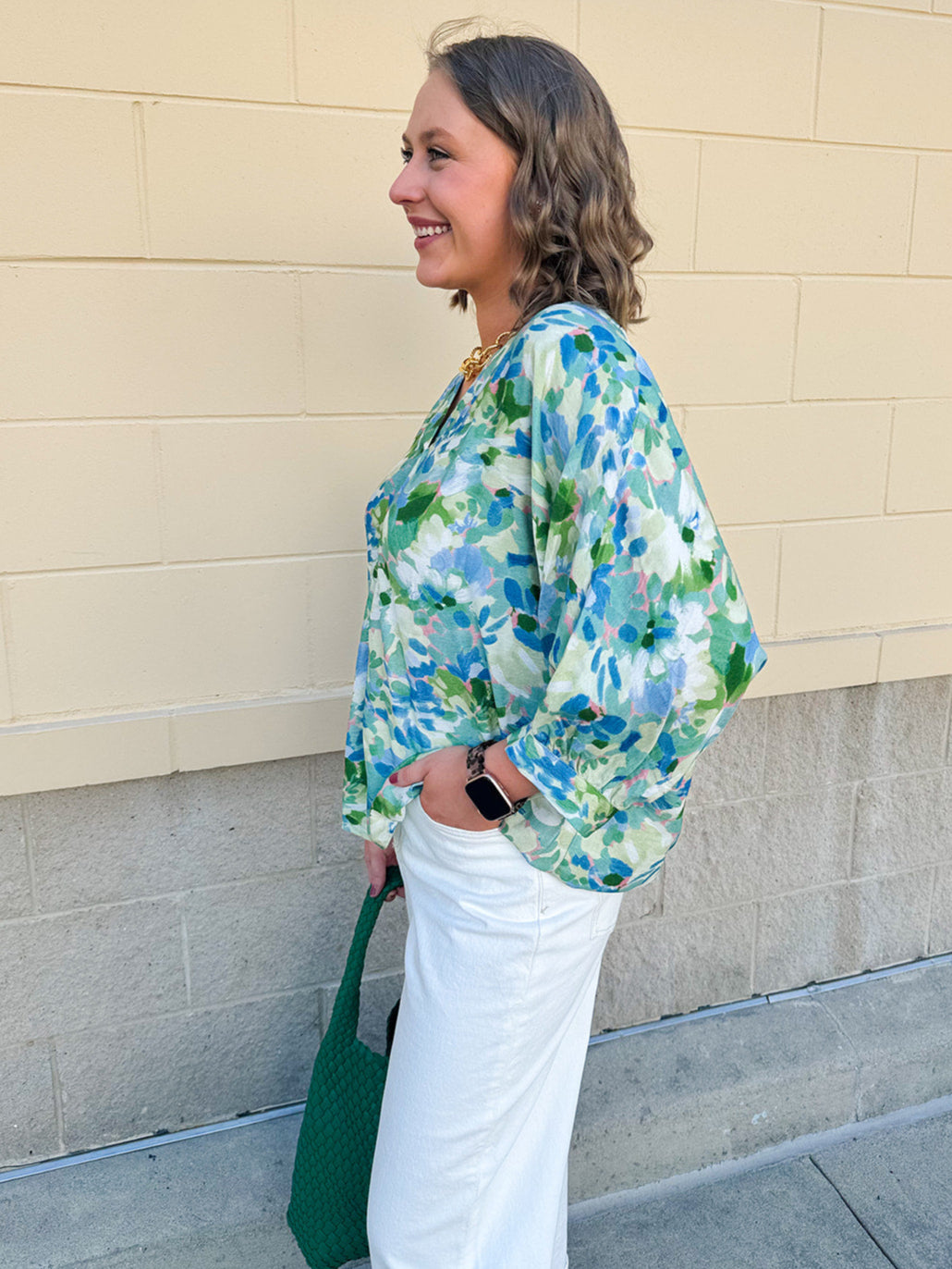 Loose-fit blouse with V-neckline and 3/4 sleeves in a pink, orange, and purple floral tie-dye print, styled for an effortless, vibrant look.