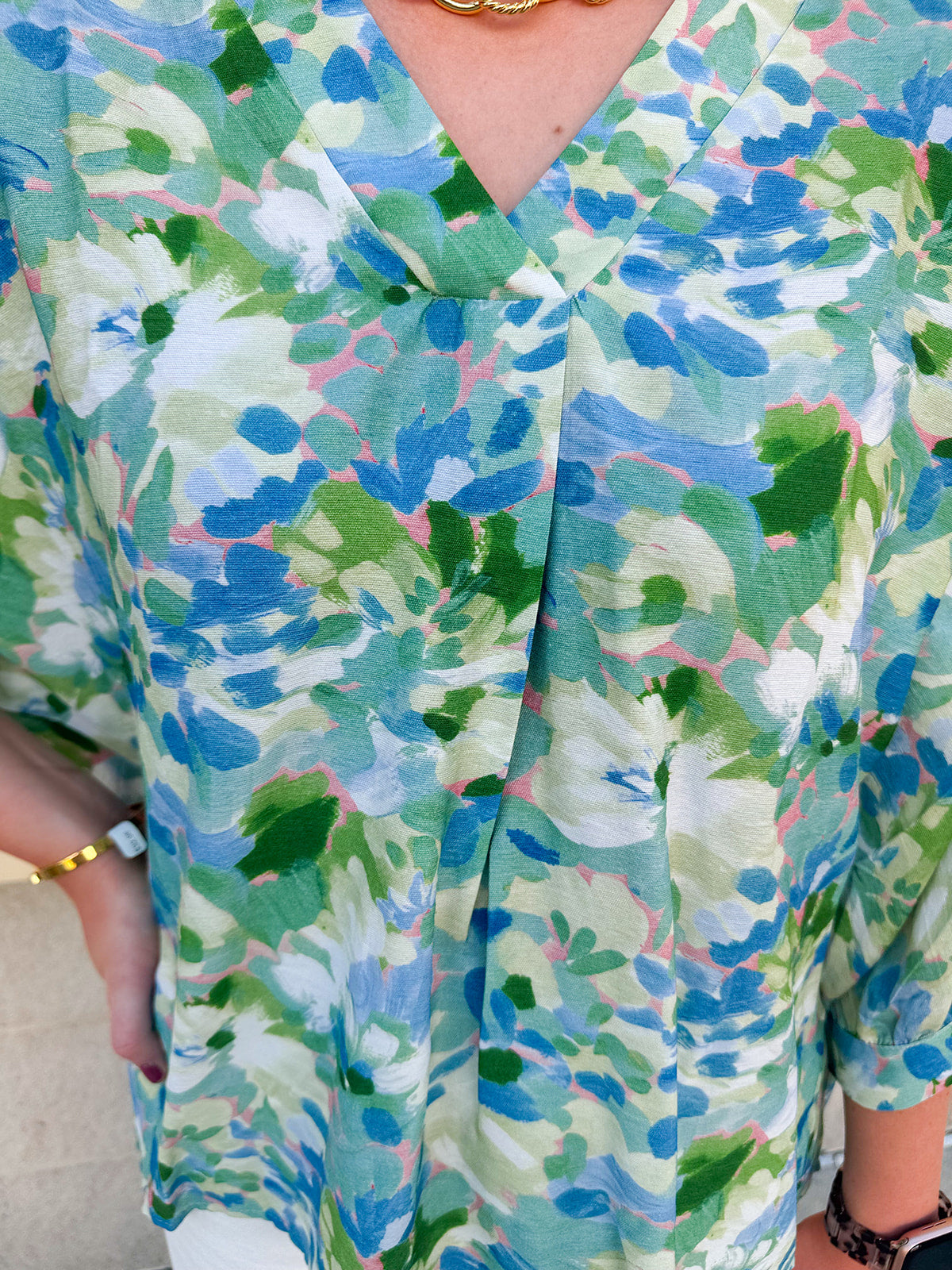 Loose-fit blouse with V-neckline and 3/4 sleeves in a pink, orange, and purple floral tie-dye print, styled for an effortless, vibrant look.