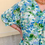 Loose-fit blouse with V-neckline and 3/4 sleeves in a pink, orange, and purple floral tie-dye print, styled for an effortless, vibrant look.