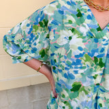 Loose-fit blouse with V-neckline and 3/4 sleeves in a pink, orange, and purple floral tie-dye print, styled for an effortless, vibrant look.