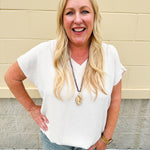 Lightweight oatmeal V-neck top with cap sleeves, styled casually for Gameday. The neutral tone and relaxed fit offer a versatile, polished look.