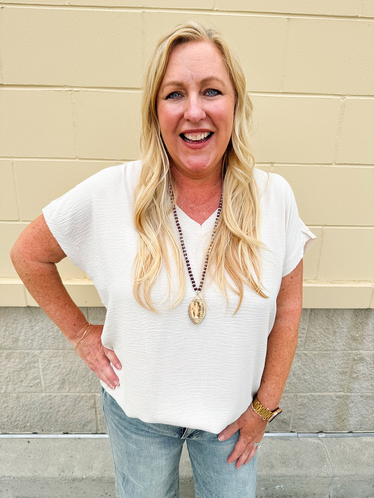 Lightweight oatmeal V-neck top with cap sleeves, styled casually for Gameday. The neutral tone and relaxed fit offer a versatile, polished look.