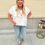 Lightweight oatmeal V-neck top with cap sleeves, styled casually for Gameday. The neutral tone and relaxed fit offer a versatile, polished look.