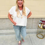 Lightweight oatmeal V-neck top with cap sleeves, styled casually for Gameday. The neutral tone and relaxed fit offer a versatile, polished look.