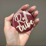 Round garnet & gold button with bold lettering, styled as a gameday accessory on bags, jackets, or outfits.