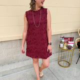 Sleeveless mini dress in rich garnet with 3D floral appliqué, scalloped embroidered hem, and side pockets. Elegant, textured, and perfect for fall or Gameday.