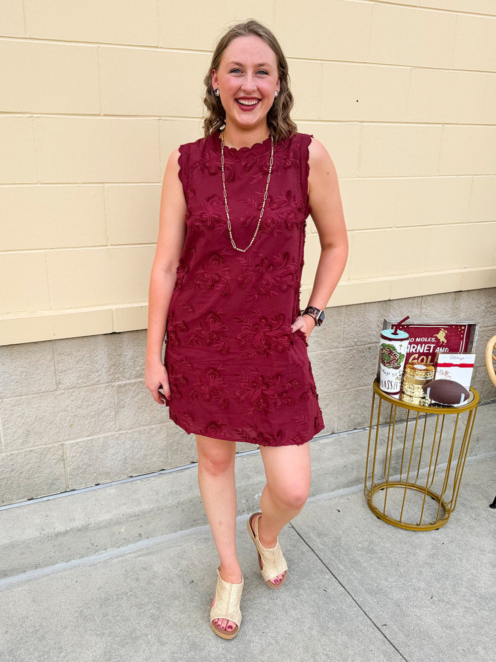 Sleeveless mini dress in rich garnet with 3D floral appliqué, scalloped embroidered hem, and side pockets. Elegant, textured, and perfect for fall or Gameday.