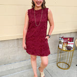 Sleeveless mini dress in rich garnet with 3D floral appliqué, scalloped embroidered hem, and side pockets. Elegant, textured, and perfect for fall or Gameday.