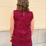 Sleeveless mini dress in rich garnet with 3D floral appliqué, scalloped embroidered hem, and side pockets. Elegant, textured, and perfect for fall or Gameday.